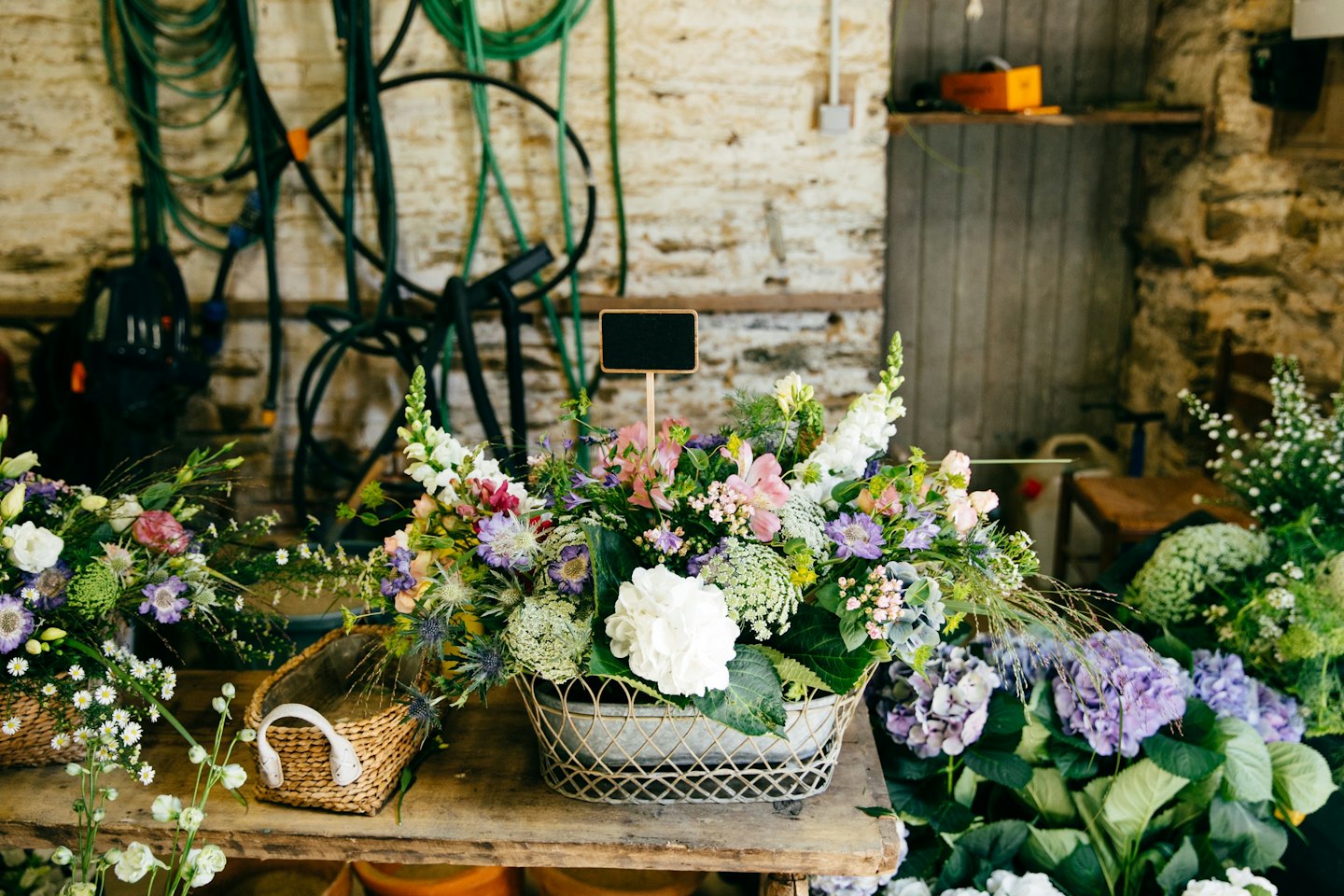 Blandade blomsterarrangemang på ett rustikt träbord med en griffeltavla.
