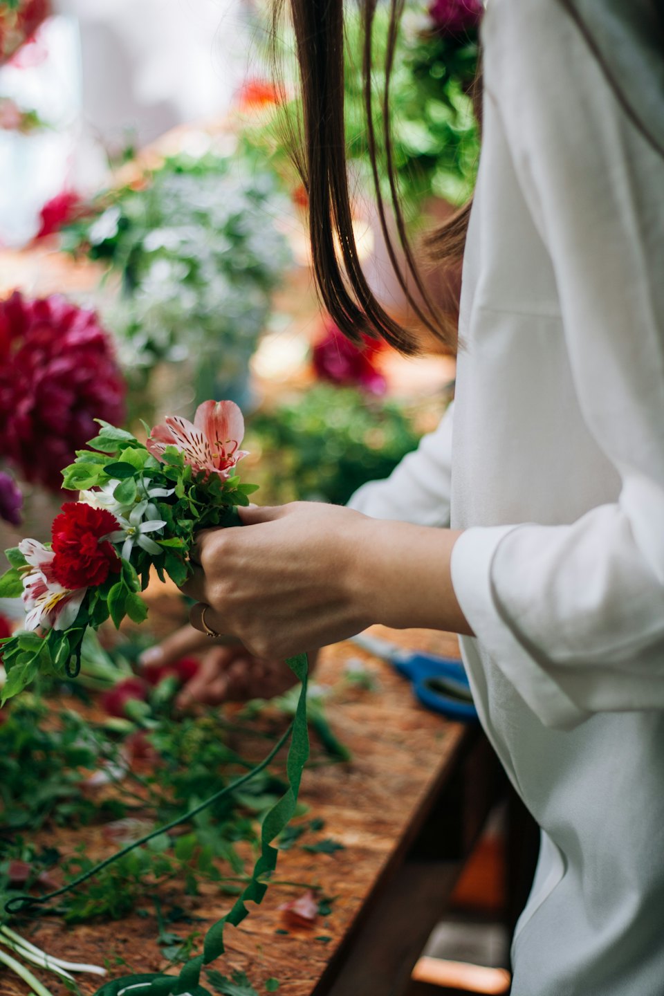 Händer som arrangerar en färgglad blomsterbukett med gröna blad.