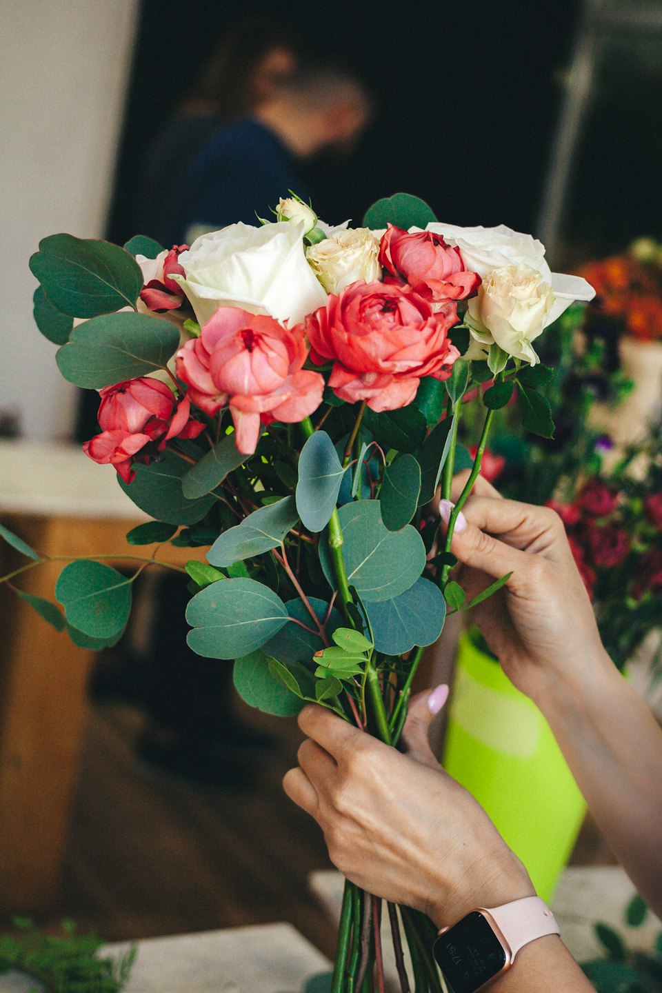 Florist som arrangerar en färgglad bukett med rosor och eukalyptusblad.